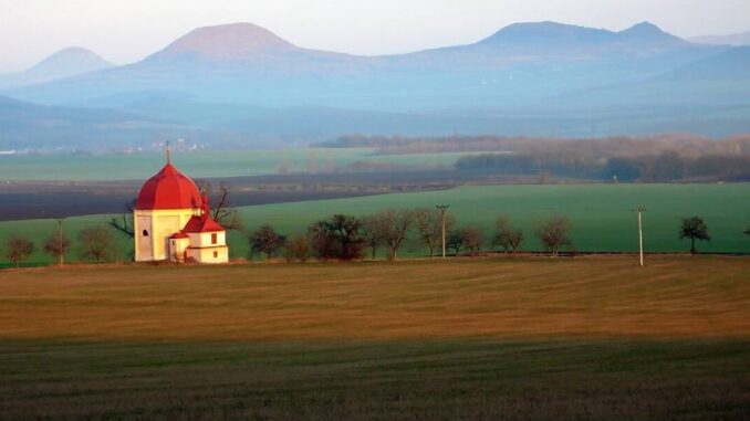 Barokní kaple ve Slavětíně a panorama Českého Středohoří. Autor: Petr Kraumann, CC BY 3.0, Wikimedia Commons